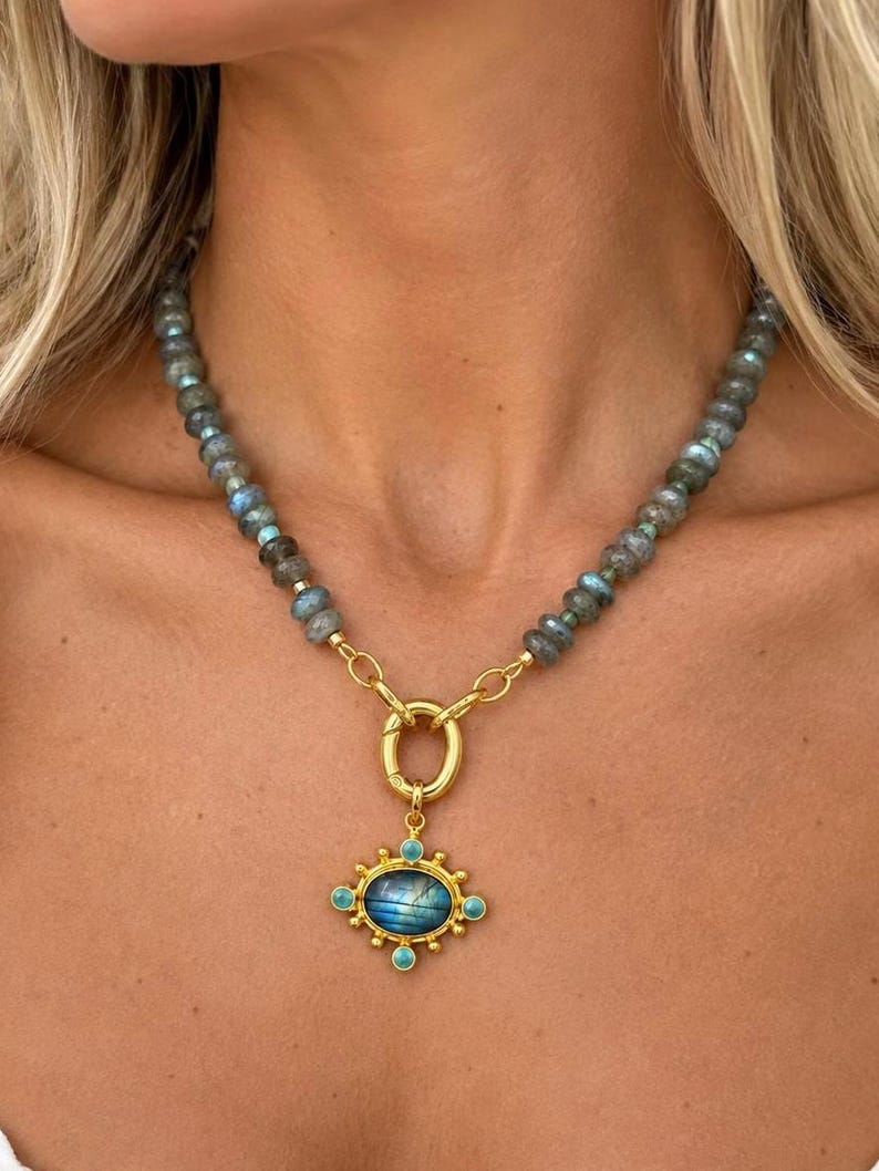 The Celeste necklace worn at the collarbone: gray labradorite beads with a gold-colored front ring and an ornate blue-green pendant.