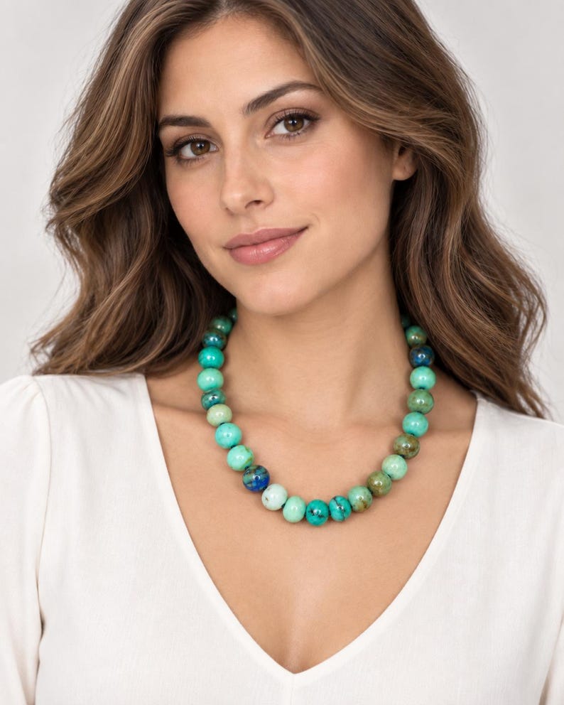 Op de afbeelding: Een kralenketting met ronde, gepolijste stenen in diverse tinten turkoois, blauwgroen en diepblauw. De kralen vertonen natuurlijke marmering en donkere aders, wat zorgt voor een uiterlijk met meerdere kleurnuances.