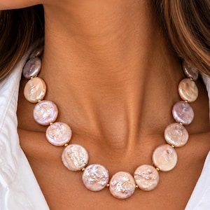 The Collette necklace worn with a white shirt: a strand of flat, round blush coin pearls with small gold-colored spacers.