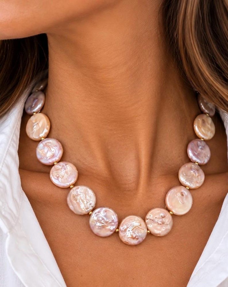 The Collette necklace worn with a white shirt: a strand of flat, round blush coin pearls with small gold-colored spacers.