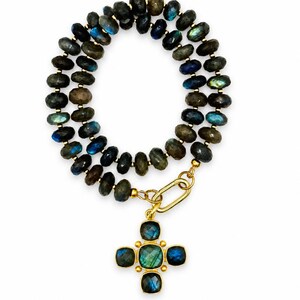 Pu&ograve; includere: Una collana a doppio filo composta da perline di labradorite sfaccettate color grigio scuro con riflessi blu e verdi iridescenti. La collana presenta una chiusura a maglia ovale in metallo dorato e un pendente a croce con cinque pietre quadrate.