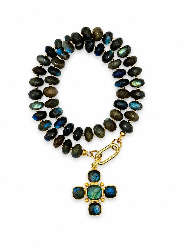 Pu&ograve; includere: Una collana a doppio filo composta da perline di labradorite sfaccettate color grigio scuro con riflessi blu e verdi iridescenti. La collana presenta una chiusura a maglia ovale in metallo dorato e un pendente a croce con cinque pietre quadrate.