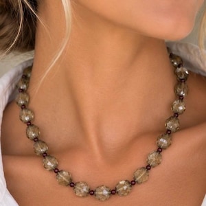 The Florence necklace worn at the collarbone: faceted smoky quartz beads alternating with small dark red garnet beads.