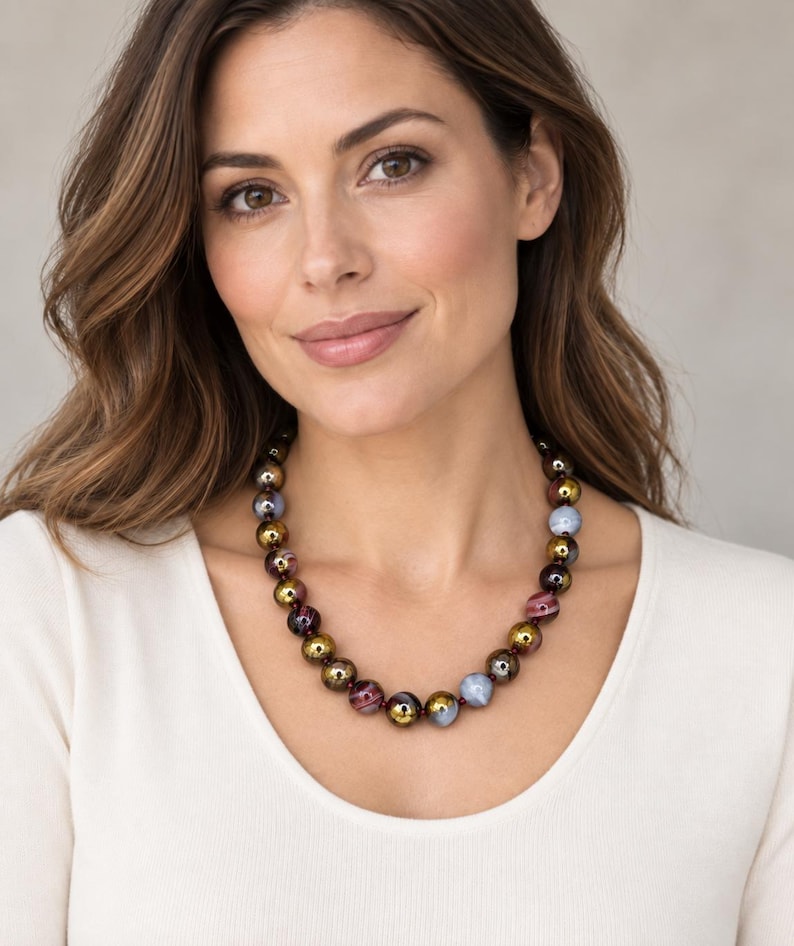 May include: A beaded necklace featuring a repeating pattern of spherical beads in metallic gold, translucent light blue, and deep burgundy with swirling marbled textures. The beads are strung together on a thin cord, creating a circular collar design.