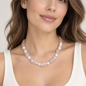 May include: A beaded necklace featuring a repeating pattern of smooth, polished rose quartz oval beads, small round white beads, and tiny pale green spacer beads. The necklace is strung on a flexible cord and sits close to the base of the neck.