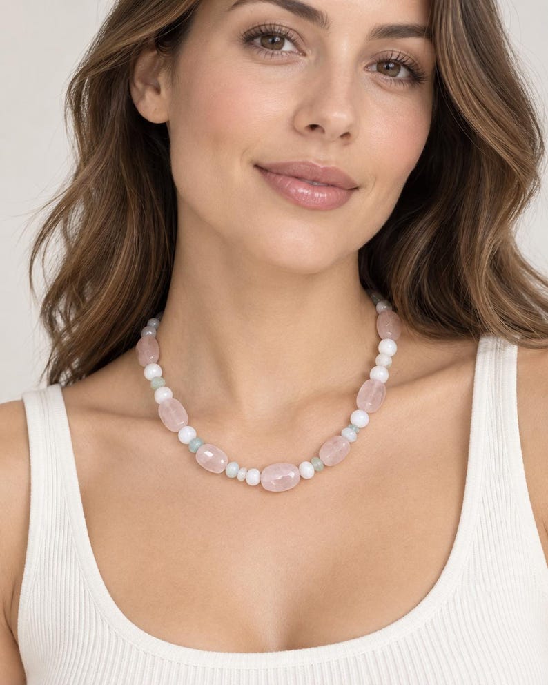 May include: A beaded necklace featuring a repeating pattern of smooth, polished rose quartz oval beads, small round white beads, and tiny pale green spacer beads. The necklace is strung on a flexible cord and sits close to the base of the neck.