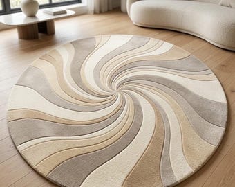 May include: A circular area rug featuring a swirling, vortex-like pattern of alternating curved bands in shades of cream, beige, taupe, and light gray. The design radiates from the center outward, creating a continuous, flowing, and symmetrical visual effect.