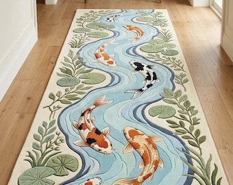 May include: A rectangular area rug featuring a winding blue river pattern with multiple koi fish in orange, white, and black. The design includes green lily pads and aquatic foliage along the edges, set against a cream-colored background.