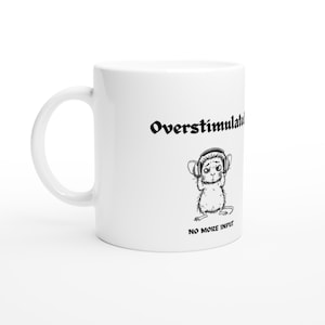 Peut inclure: Un mug en céramique blanche avec un dessin noir représentant une souris portant un casque audio. Au-dessus de la souris, le texte "Overstimulated" est écrit en police gothique. En dessous, le texte "NO MORE INPUT" est en police sans empattement.