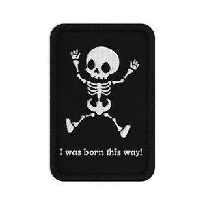 Peut inclure: Un écusson rectangulaire brodé noir représentant un squelette blanc avec les bras et les jambes levés dans une pose sautillante. Sous le squelette, le texte "I was born this way!" est brodé en blanc, le tout dans une bordure noire.