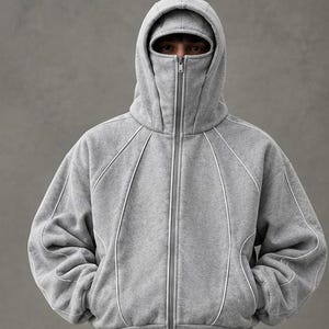May include: A heather grey zip-up hoodie featuring a high-neck collar that covers the lower face and a built-in hood. The garment is detailed with white piping along the seams, creating curved lines across the chest and sleeves.