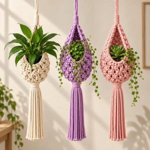 Könnte beinhalten: Drei Makramee-Pflanzenhänger in Creme, Lavendel und Altrosa. Jeder tropfenförmige Halter verfügt über ein geknotetes Kordeldesign, eine lange dekorative Quaste am unteren Ende und eine Aufhängeschlaufe oben, die jeweils eine grüne Topfpflanze enthalten.