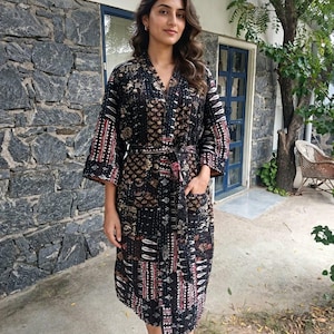 May include: A knee-length robe featuring a dark black base with a multi-coloured patchwork pattern in shades of red, white, and brown. The garment includes long sleeves, a tie-waist belt, and two front pockets, constructed with visible stitching.