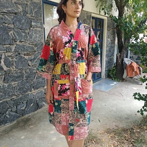 Könnte beinhalten: Ein knielanger Morgenmantel im Kimono-Stil mit einem Patchwork-Design aus verschiedenen Blumen- und geometrischen Mustern in den Farben Rot, Gelb, Rosa, Grün und Schwarz. Der Mantel hat lange Ärmel, einen Bindegürtel und zwei aufgesetzte Taschen.