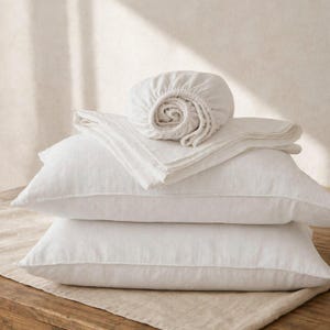 Peut inclure: Un ensemble de linge de lit blanc composé de deux oreillers rectangulaires et d'un drap-housse plié. Les articles sont fabriqués dans un tissu texturé avec des motifs de tissage visibles. Le drap-housse est roulé sur le dessus des oreillers.