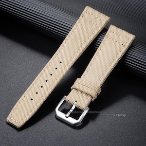 May include: A beige watch strap made of a woven fabric material featuring a silver-toned metal buckle and a series of punched holes for adjustment. The strap has visible stitching along the edges and includes the text HQstrap printed on the surface.