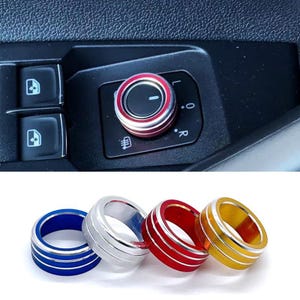 May include: A set of four circular metal knob covers with a textured knurled edge and two thin horizontal grooves. The covers are available in blue, silver, red, and gold. One red cover is shown installed on a car side mirror adjustment dial.