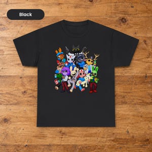 Puede incluir: Una camiseta negra de manga corta con un estampado gráfico colorido de varios personajes animales de dibujos animados con ropa médica y de seguridad. El diseño incluye figuras con astas, orejas de conejo y rasgos felinos en grupo.