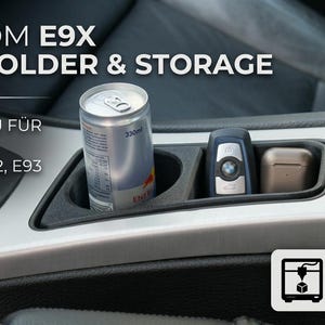 May include: A black custom E9X cup holder and storage insert for BMW 3 series E90, E91, E92, and E93 vehicles. The unit is installed in the center console, holding a silver beverage can, a car key fob, and a small rectangular case.