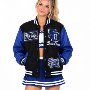 以下が含まれることがあります： 白のストライプ入りリブ袖と襟、青い袖、そしてBig Raji、SD Bucc Cheer、Bucs Cheerと書かれたラインストーン付きのワッペンが特徴の黒と青のバーシティジャケット。白と青のチアリーダーユニフォームの上に着用。