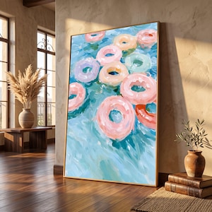 Peut inclure: Une peinture encadrée rectangulaire représentant plusieurs bouées de piscine gonflables colorées flottant sur une eau bleue texturée. L'œuvre présente des nuances de rose, pêche, lavande et vert menthe avec des coups de pinceau visibles.