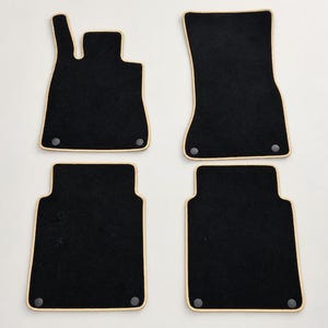 Peut inclure: Un ensemble de quatre tapis de sol automobiles noirs avec une bordure en tissu beige. Chaque tapis comporte des clips de fixation circulaires gris foncé aux coins, conçus pour une installation sécurisée dans l'habitacle.