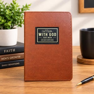 May include: A brown leather-textured devotional book with a black rectangular label on the front cover. The label features the white and gold text: One Minute WITH GOD FOR MEN 365 DAILY DEVOTIONS. The book is positioned upright on a wooden surface.