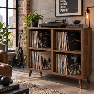 May include: A dark wood four-compartment record storage cabinet with tapered legs, filled with vinyl records including John Coltrane, Pink Floyd, Fleetwood Mac, and The Beatles. A black turntable sits on top, alongside two books and a small bowl.