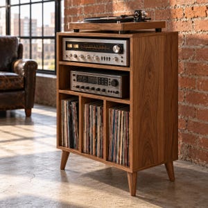 May include: A wooden record player stand with four tapered legs, featuring a top surface for a turntable, two open shelves housing audio receivers with silver knobs and dials, and three lower compartments filled with vinyl records.