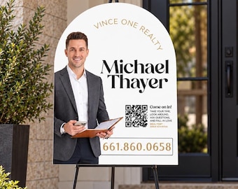 May include: An arched white real estate sign on a black tripod stand featuring a photo of a person in a gray suit, the text Vince One Realty, Michael Thayer, a QR code with the text Come on in, and the phone number 661.860.0658.