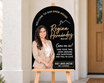 May include: An arched black open house sign on a wooden easel featuring a photo of a person in a beige blazer, the text "WELCOME TO OUR OPEN HOUSE", "Regina Hernández REALTOR", "Come on in!", "TAKE YOUR TIME, LOOK AROUND, ASK QUESTIONS, AND FALL IN LOVE", "661.860.0658", and "DRE # 44329842".