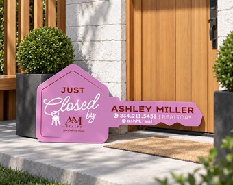 May include: A pink key-shaped real estate sign featuring the text JUST Closed by, AM REALTY, ASHLEY MILLER, 234.211.5432, REALTOR, and @ashM.real. The sign includes a graphic of a set of keys and is positioned on a concrete porch.