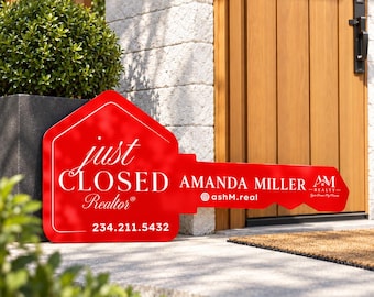 May include: A large red key-shaped sign with white text reading just CLOSED Realtor, AMANDA MILLER, the Instagram handle ashM.real, and the phone number 234.211.5432. The sign features a small white logo with the letters AM.