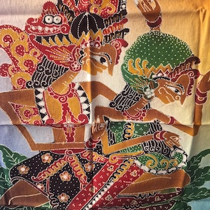 Può includere: Un tessuto con una colorata stampa batik di due figure stilizzate nello stile tradizionale delle marionette d'ombra indonesiane. Le figure sono decorate con motivi complessi in rosso, verde, giallo e nero su uno sfondo sfumato.
