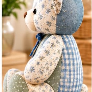 May include: A stuffed teddy bear shown from the side, featuring a patchwork design of blue and white floral fabric, blue gingham check, and green fabric with white polka dots. The bear has a brown nose and a small blue ribbon tied at the neck.