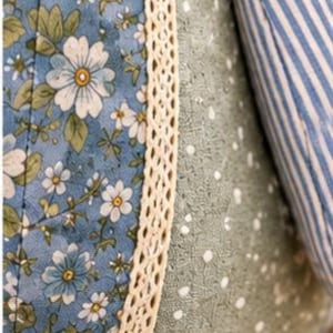 May include: A quilted fabric object featuring panels of blue floral print, sage green fabric with white dots, and blue and white stripes. A cream-coloured lace trim separates the panels. The text 7. Fabric & Stitching is printed at the bottom.