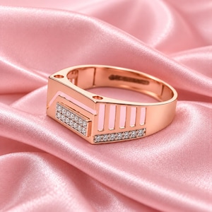 May include: A rose gold ring featuring a rectangular face with two rows of small clear stones, accented by a geometric cutout design along the side and a row of small clear stones embedded along the lower band edge.