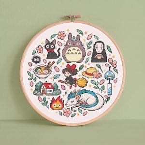 May include: A circular wooden embroidery hoop containing a cross-stitch pattern featuring various animated characters, a bowl of ramen, a small house, a fire spirit, a straw hat, and a wind chime, all surrounded by pink cherry blossom flowers.