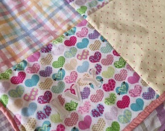 May include: A patchwork quilt featuring squares of pastel plaid, yellow fabric with small red dots, and a white background printed with multicoloured hearts in pink, blue, green, and purple. The name IVY is appliqued in white letters.