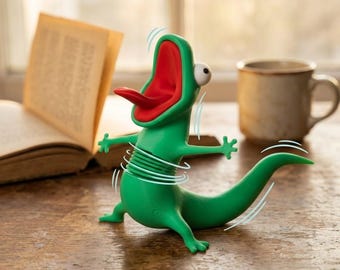 Könnte beinhalten: Eine grüne Echsenfigur mit weit geöffnetem rotem Maul, herausgestreckter Zunge und einem großen weißen Auge. Der Körper hat einen federartigen Mittelteil, und die Figur ist mit Bewegungslinien dargestellt, die ein Vibrieren oder Schütteln andeuten.