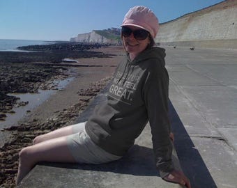 May include: An olive green hooded sweatshirt featuring a front kangaroo pocket and white text that reads "THREW UP, NOW I FEEL GREAT." The garment is paired with a light-colored cap and dark sunglasses, creating a casual look for outdoor wear.