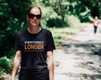 May include: A black short-sleeved t-shirt featuring the white text "EVERYTHING'S" above the orange text "LONGER" with a dashed orange line underneath. The shirt has a crew neckline and is made of a solid black fabric with a standard fit design.