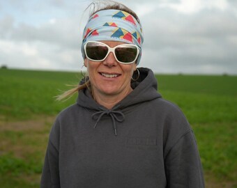 May include: A charcoal gray hooded sweatshirt with a subtle embroidered logo on the chest, paired with a light blue tubular bandana featuring a repeating pattern of red, yellow, and blue triangles and the text Trail Guides in white lettering.