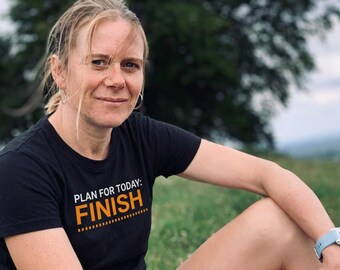 May include: A black short-sleeved t-shirt featuring the white text "PLAN FOR TODAY:" above the large orange text "FINISH" with a dashed line underneath. The shirt is made of a solid black fabric and has a standard crew neckline and short sleeves.