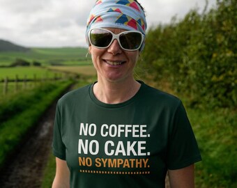 May include: A dark green short-sleeved t-shirt featuring the white text NO COFFEE. NO CAKE. and the orange text NO SYMPATHY. with a dashed line underneath. The shirt is worn with a light blue patterned headband and white-framed sunglasses.