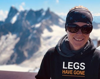 May include: A black hooded sweatshirt featuring the white text LEGS and the orange text HAVE GONE printed on the front. The garment is worn with a dark gray headband patterned with small stars and dark-tinted sunglasses with black frames.