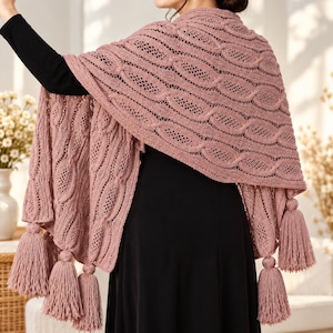 May include: A dusty rose knitted shawl featuring an intricate cable knit pattern combined with openwork lace sections. The triangular-shaped garment is finished with multiple matching yarn tassels attached along the bottom edges.
