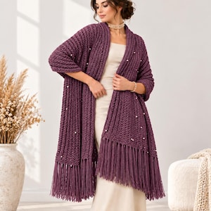 May include: A long, deep purple open-front cardigan featuring a chunky ribbed knit texture, long sleeves, and a fringe hem. The garment is embellished with scattered white faux pearls throughout the front panels and sleeves, creating a textured look.