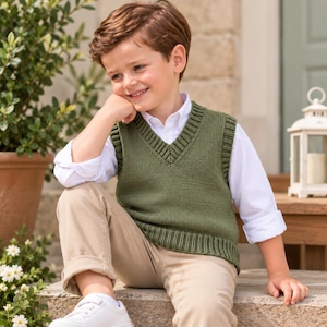 May include: An olive green V-neck sweater vest featuring a ribbed knit neckline and hem, worn over a crisp white long-sleeved button-down shirt paired with tan trousers and white sneakers, creating a layered outfit for a child.