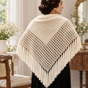 May include: A cream-colored triangular shawl featuring a solid knit upper section and a decorative openwork crochet pattern on the lower half, finished with long, straight fringe tassels along the bottom edges of the garment.